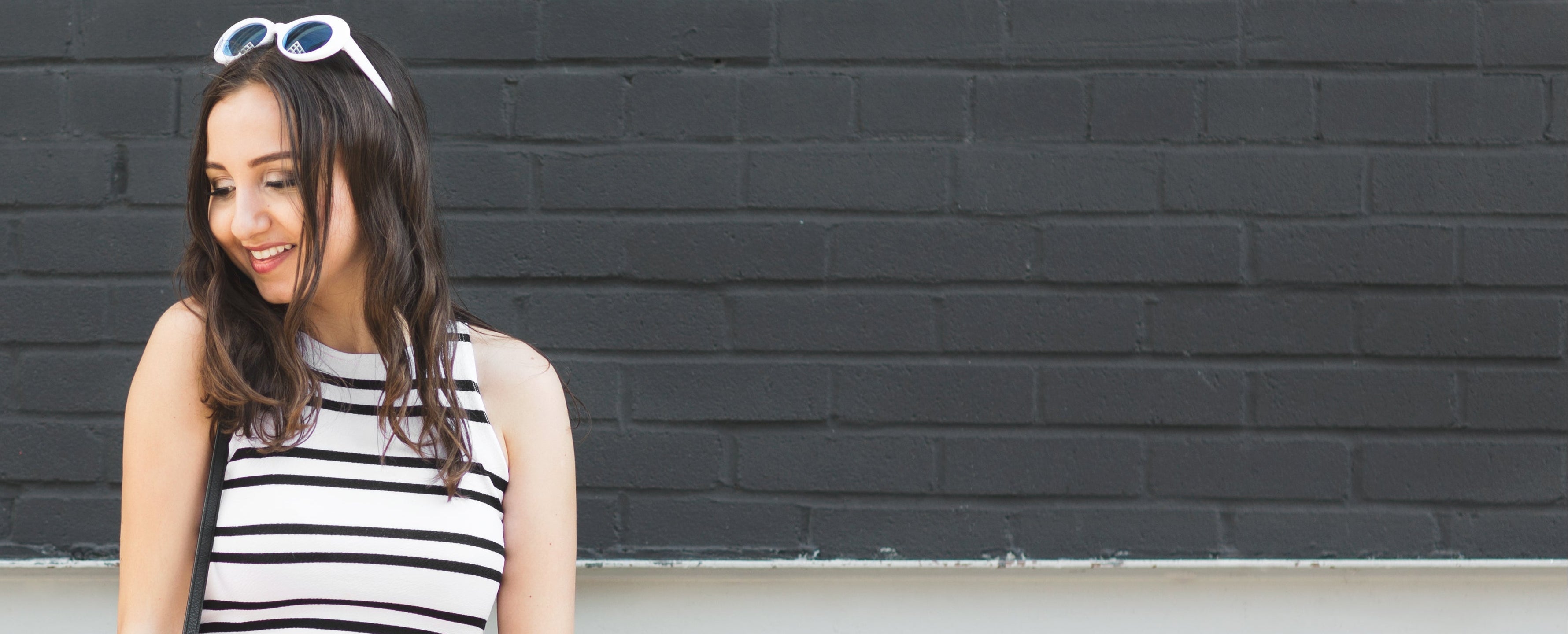 Woman wearing a black and white striped sleeveless top and red shorts standing against a black brick wall.